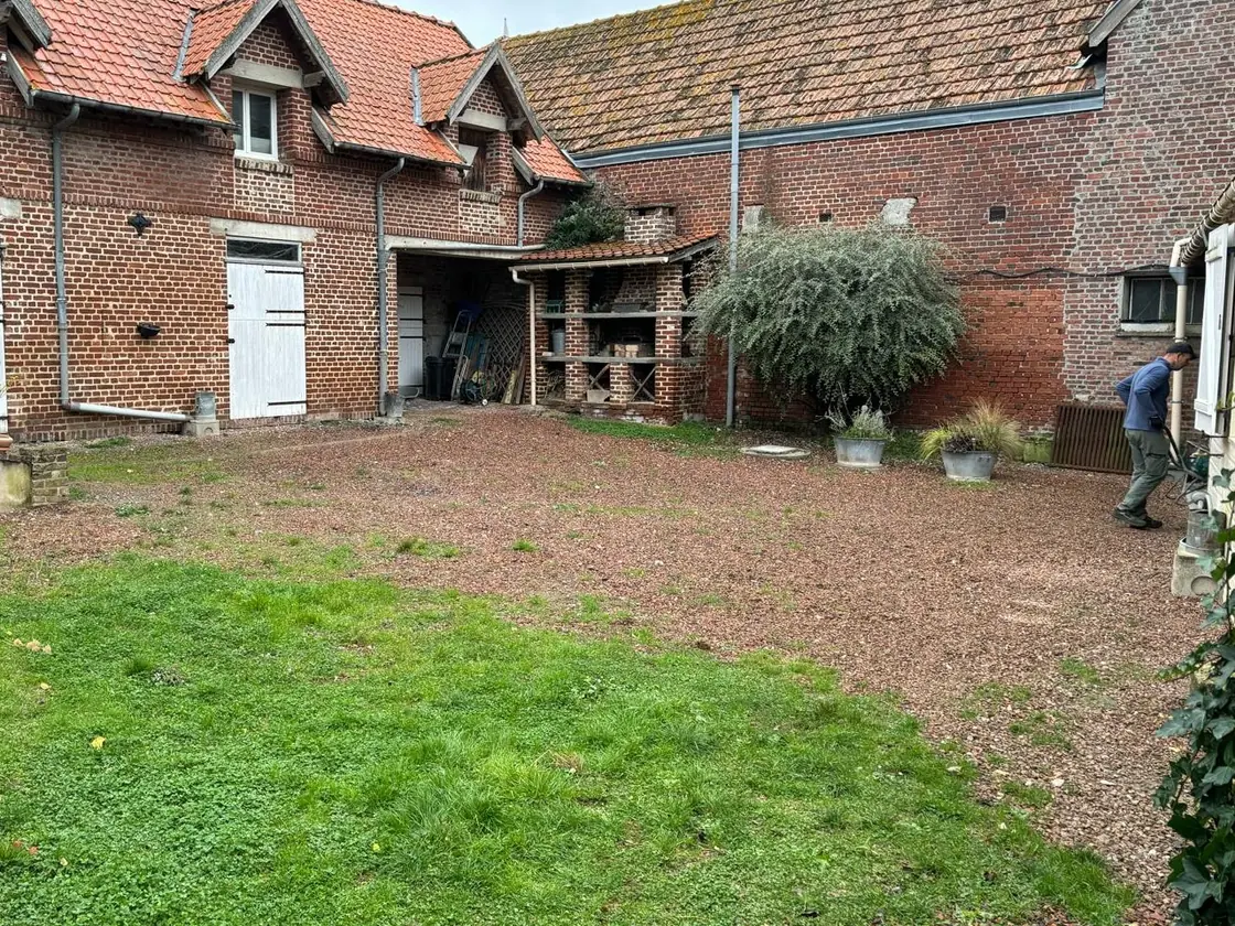 La même cour de ferme, entièrement recouverte de gravillon clair et nivelée — avant