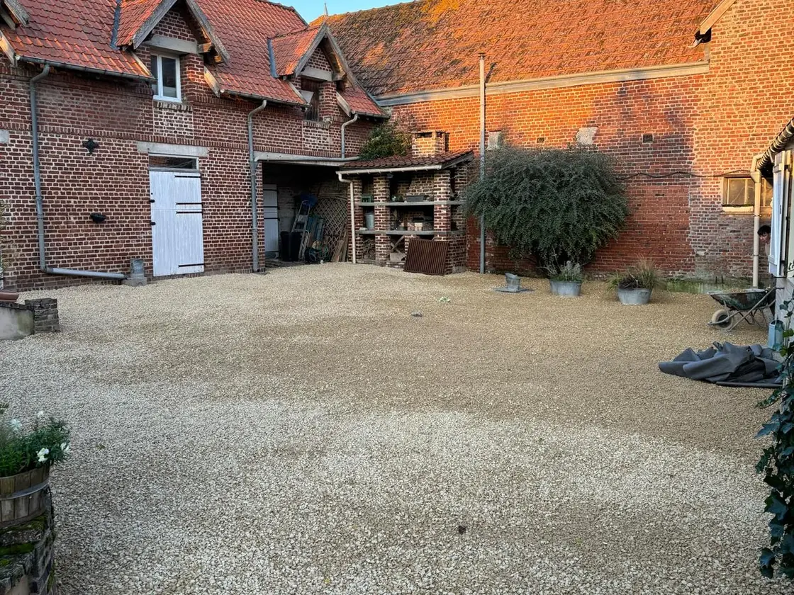La même cour de ferme, entièrement recouverte de gravillon clair et nivelée — après