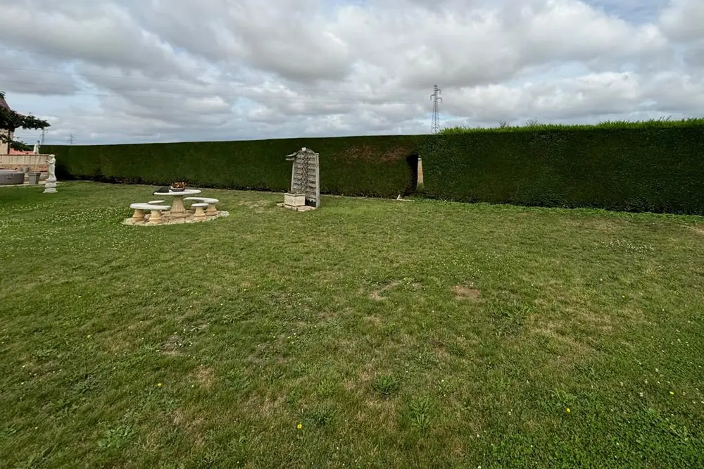 Grande pelouse tondue devant une longue haie taillée, table et bancs de jardin en pierre