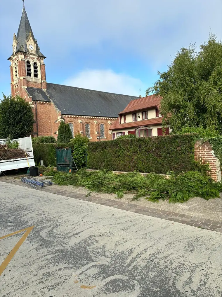 Haie taillée devant une église, branches coupées rassemblées le long du trottoir