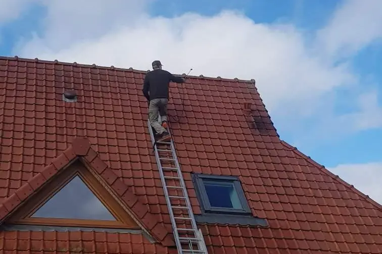 Intervenant sur une toiture en tuiles rouges, échelle de couvreur posée sur le rampant